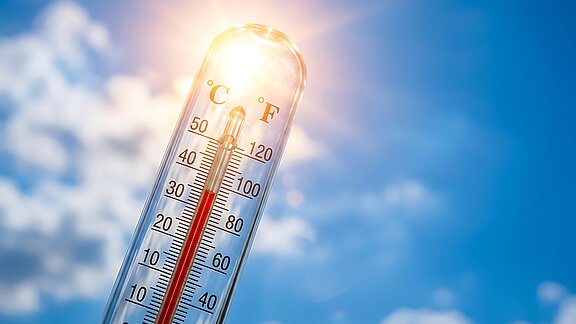 Close up thermometer indicating high temperature under bright summer sun against blue sky showing concept of global warming heat wave climate crisis environmental danger.