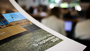 Dossier de presse en premier plan avec les élus dans l'hémicycle en second plan