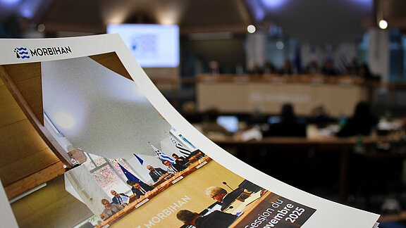 Dossier de presse de session en premier plan et hémicycle avec les élus pour le deuxième 