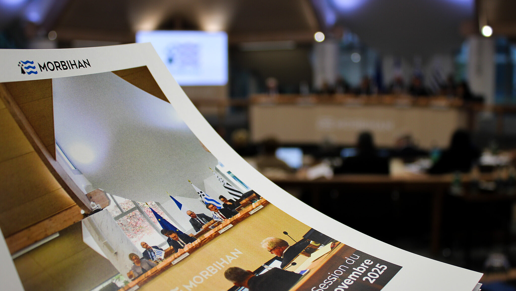 Dossier de presse de session en premier plan et hémicycle avec les élus pour le deuxième 