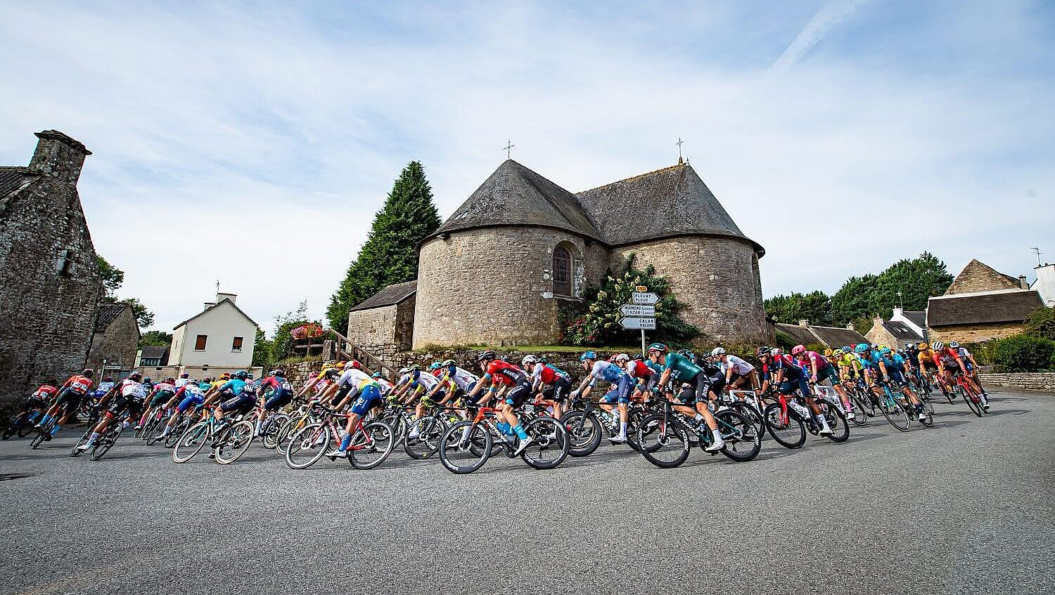 Plusieurs cyclistes participant à la course du Grand Prix de Plouay passant devant une église de village
