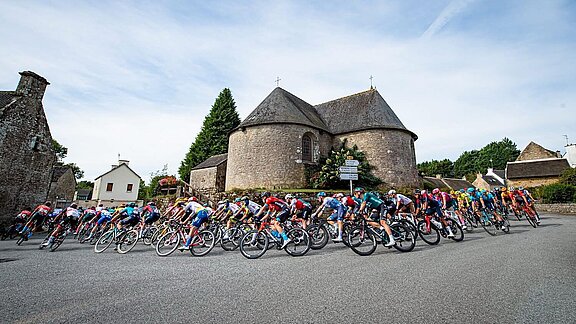 Plusieurs cyclistes participant à la course du Grand Prix de Plouay passant devant une église de village